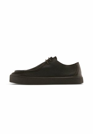 Zwarte lage sneaker met gestructureerd leren bovenwerk, veters aan de voorkant en dikke rubberen zool, zijaanzicht op een witte achtergrond.