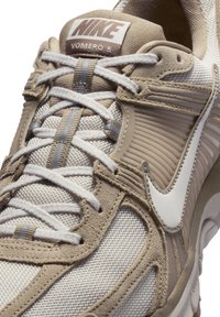 Nike Vomero 5 sportcipők bézs és krémszínben. Háló és velúr anyagokkal készült, rétegezett designnal, feltűnő fűzőkkel és a jellegzetes pipa részlettel.