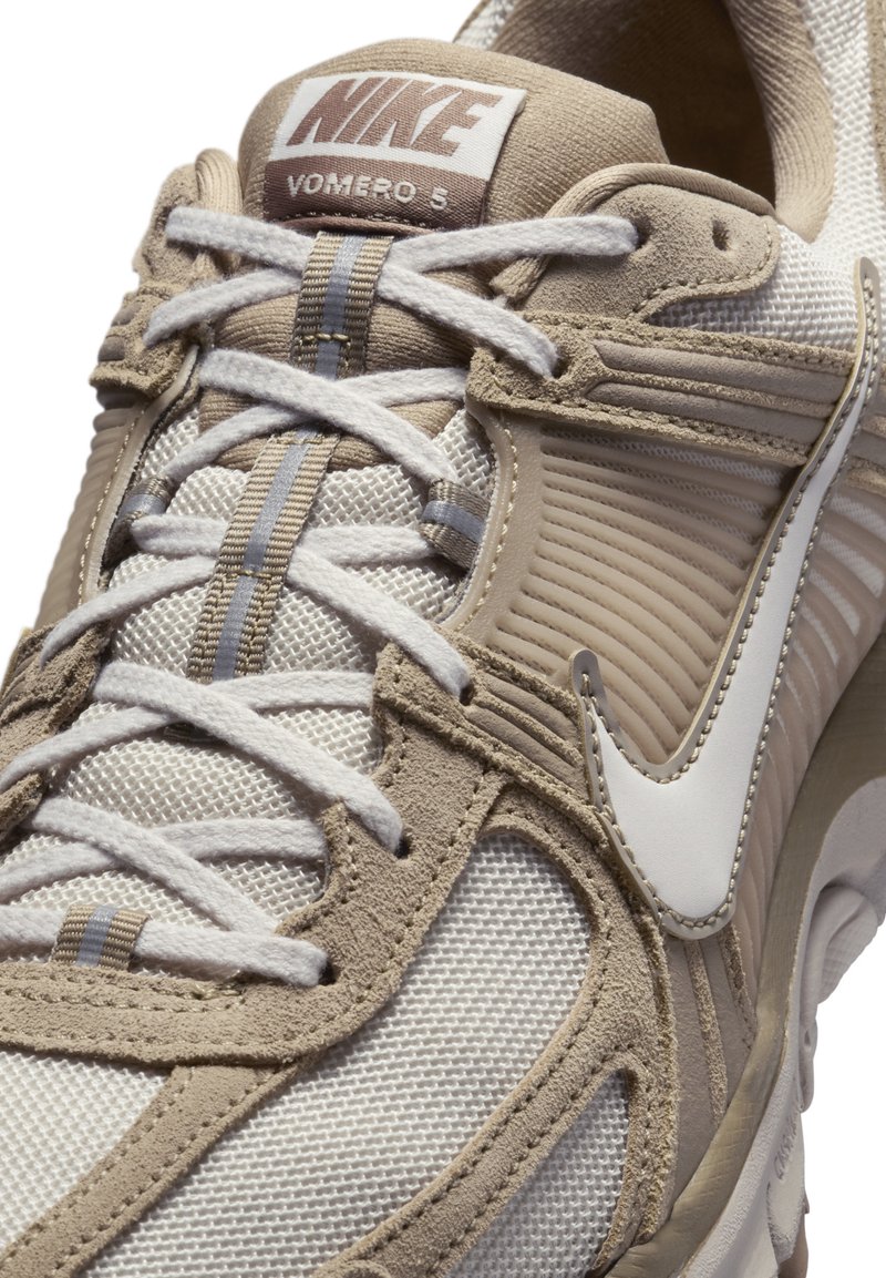 Zapatillas Nike Vomero 5 en beige y crema. Presentan materiales de malla y gamuza, un diseño en capas, cordones prominentes y el distintivo logo de swoosh.
