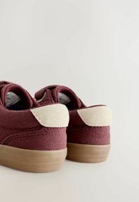 Bordeaux sko med en beige krave og gummisål, vinkelret for at vise bagsiden mod en lys baggrund.