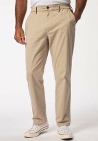 Chino beige con vita e passanti per cintura, dotati di chiusura con bottone e tasche laterali, abbinati a sneakers bianche.