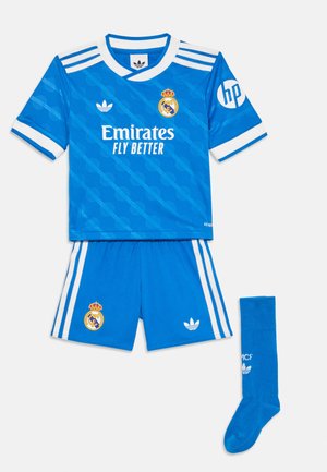 Maillot de football bleu du Real Madrid avec des détails blancs, rayures Adidas, sponsor Emirates Fly Better, et chaussettes bleues assorties avec logos blancs.