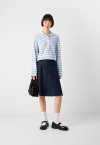 Lyseblå langermet stripete polo, mørk denim A-linje skjørt, svart håndveske, hvite sokker, svarte Mary Jane-sko. Enkelt, moderne design.