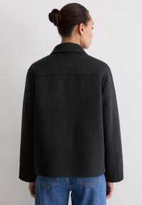 Czarna kurtka z mieszanki wełny o strukturalnym kroju, z kołnierzem i długimi rękawami, zestawiona z jasnoniebieskimi dżinsami.