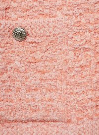 Teksturenan roza pletenina z vzorom in srebrnim ovalnim gumbom kot dodatkom. Površina se zdi mehka in rahlo puhasta.