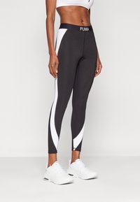 Leggings neri con pannelli laterali bianchi, caratterizzati da un design aderente e un logo PUMA in vita. Tessuto liscio e materiale elasticizzato.