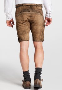 Pantalones cortos de cuero marrón con costuras decorativas en la parte posterior. Llevados con calcetines de punto oscuros y zapatos marrones. Los pantalones cortos tienen una textura suave.