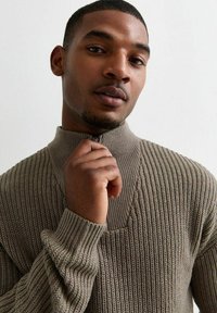 Olive green, ribbed knit sweater with a high collar and a V-cut neckline. Textured fabric with long sleeves, fitted cuffs, and a relaxed fit.