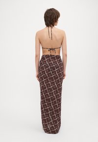 Brun mønstrede maxiskørt med halterneck top, der har et geometrisk hvidt design, lavet af letvægtsstof.