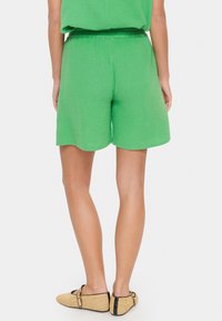 Zelena teksturirana kratka hlače s udobnim krojem in elastičnim pasom, v kombinaciji s bež tkanimi balerinkami z črnim trakom in zaponko.