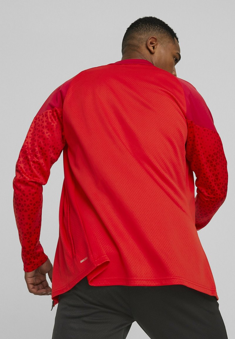 Rotes Sportshirt mit langen Ärmeln, strukturiertem, einfarbigem Körper und gemusterten Ärmeln. Mit abgerundetem Saum und einem seitlichen Reißverschlussdetail nahe dem unteren Ende.