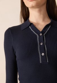 Polo à manches longues côtelé bleu marine avec un col, doté d'une patte de boutonnage et d'accents rayés contrastants à côté des boutons.