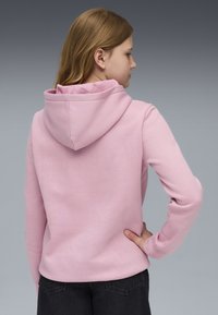 Rosa Kapuzensweatshirt aus weichem Stoff, mit lockerer Passform, langen Ärmeln und einem detaillierten Kapuzendesign. Tragen mit dunklen Jeans.