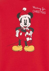 Sweat-shirt rouge avec un graphique d'une souris dessin animé portant un chapeau de Noël et une écharpe, avec des chaussures jaunes, légendé "En attendant Noël".