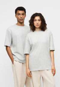 Γκρι βαμβακερά μπλουζάκια με κοντά μανίκια, άνετη γραμμή, στρογγυλή λαιμόκοψη, φορεμένα από δύο μοντέλα. Το φόντο είναι λευκό για αντίθεση.