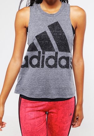 Kobieta w szarym, bezrękawnym topie Adidas na czarnym sportowym biustonoszu i czerwonych legginsach w wzory z czarnymi bocznymi paskami.
