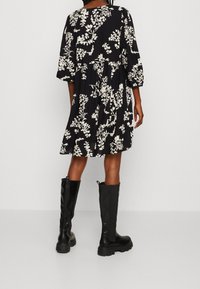 Robe noire à fleurs avec des motifs de fleurs blanches, manches courtes bouffantes, taille froncée et ourlet à hauteur des genoux, accompagnée de bottes noires à hauteur des genoux.