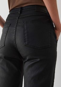 Black denim jeans with a fitted waist, back pockets, and a smooth texture. Features subtle stitching and a standard belt loop design.