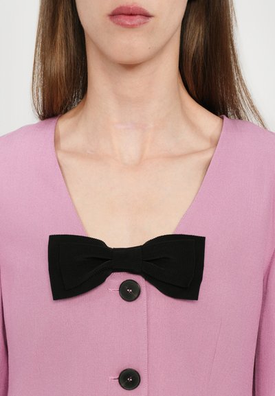 Light pink dress featuring a deep V-neck, black ribbon bow at the chest, and three black buttons along the front. Smooth fabric texture.
