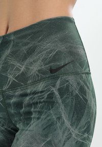 Groene fitnessleggings met een gestructureerd ontwerp, voorzien van een licht patroon, een hoge tailleband en een klein zwart Nike-logo.