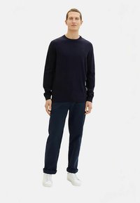 Mörkblå långärmad tröja i mjukt material, kombinerad med mörka byxor och vita sneakers. Enkel, klassisk design med en rund halsringning.