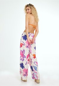 Multifarvet blomsterprint bukser med en lys cremefarvet baggrund, løst fit og elastisk talje; modellen har en orange top med knyt bagpå på.