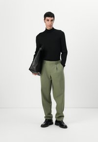 Black long-sleeve turtleneck, light green tailored trousers, and black leather shoes. Model holds a black leather bag. Simple, structured look.