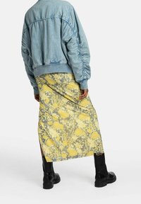 Giacca bomber azzurro chiaro con texture trapuntata abbinata a una gonna midi a stampa floreale gialla. Stivali neri alla caviglia con suola spessa.