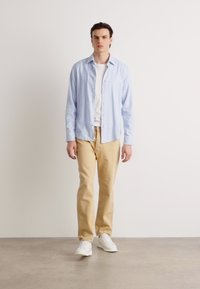 Cămașă bleu deschis cu nasturi, tricou alb dedesubt, pantaloni bej, adidași albi; textură netedă, croială lejeră, design casual.