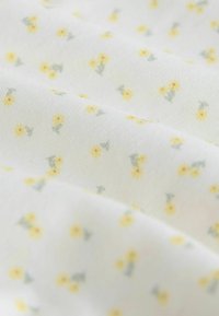 Tissu blanc avec de petits regroupements dispersés de fleurs jaunes et de feuilles vertes dans un motif délicat et répétitif.