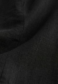 Tessuto di lino nero con una superficie strutturata, caratterizzato da sottili variazioni nella trama e una leggera lucentezza, che cade dolcemente in pieghe.