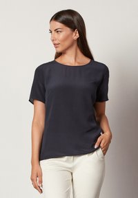 Marineblå kortærmet bluse i let materiale med rund hals, glat tekstur og afslappet pasform, parret med lyse bukser.