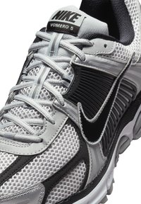 Nike Vomero 5 tekaški čevlj je izdelan iz mrežaste zgornjega dela v sivi in črni barvi, ima oblazinjeno podplato in ojačan sistem vezalk za podporo in zračnost.