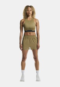 Conjunto deportivo que incluye un sujetador deportivo ajustado de color verde oliva con detalles en negro y pantalones cortos holgados a juego, complementados con zapatillas y calcetines blancos.