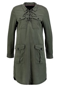 Olivově zelená bunda s dlouhými rukávy, dvěma náprsními kapsami a stahováním u krku na šňůrku. Vyrobená z hladké látky s volným střihem.