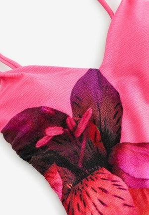 Pink fabric top featuring a floral design with large purple and red flowers. Textured surface with thin straps and a fitted shape.