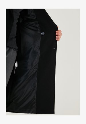 Palton negru cu o captuseală netedă, având închidere cu nasture și buzunare laterale. Exteriorul are o finisare texturată și un design minimalist.