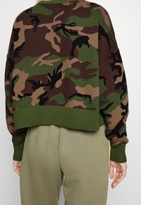 Cropped pullover in camouflage print featuring shades of green, brown, and black, with ribbed cuffs and hem, made from soft fabric.