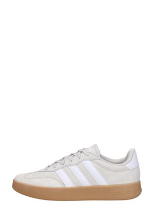Zapatilla Adidas de perfil bajo en ante gris claro con rayas blancas y suela de goma color caramelo, mostrada de perfil hacia la izquierda.