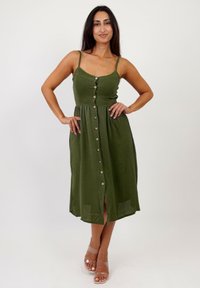 Vestido midi sin mangas en color verde oliva con frente abotonado y cintura fruncida. Hecho de una tela ligera, con una textura sutil y una abertura lateral.