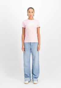 Světle růžové bavlněné tričko s krátkým rukávem, se bílým logem. V kombinaci se světle modrými širokými džínami a bílými teniskami.