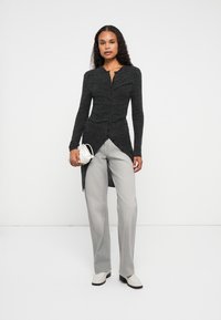 Cardigã cinza de mangas longas com fecho de botão, tecido texturizado e bainha assimétrica. Combinado com calças largas cinza claro e sapatos brancos.