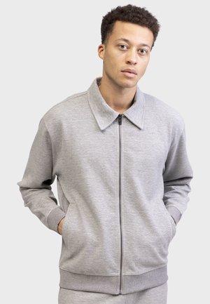 Gray zip-up jacket with a thick ribbed texture, large collar, and side pockets, featuring a relaxed fit and elastic cuffs.