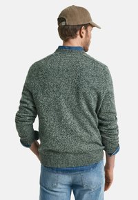 Grüner gestrickter Pullover mit einem strukturierten Muster, gerippten Bündchen und Saum, über einem blauen Jeanshemd getragen. Verfügt über eine hellbraune Mütze.