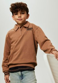 Ruda džemperio tipo su užtrauktuku ir apykakle, ant kurios parašyta „Tournament Tennis“. Minkšta medžiaga, ilgos rankovės ir matoma dryžuota apvado detalė juosmens srityje.