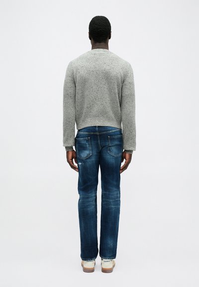 Grijze gebreide trui met een ronde hals, gecombineerd met blauwe denim jeans met een lichte vervaging en twee achterzakken. Tan casual schoenen maken de look compleet.