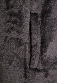Gros plan sur une poche en tissu polaire gris foncé texturé avec une ouverture verticale et une surface douce et duveteuse.