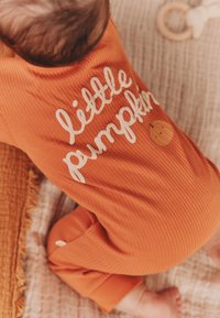 Combinaison pour bébé orange à rayures avec du texte blanc indiquant "petit potiron" et un petit graphique de potiron, présentant des poignets ajustés et un tissu doux.
