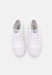 Pair of white Adidas high-top sneakers with white laces, Adidas logo on tongue, and textured rubber soles on white background.