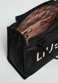 Borsa in tessuto nero con chiusura a zip, dotata di una foderatura interna rosa chiaro e tasca. La parte esterna mostra "LIU JO" in caratteri in grassetto.